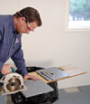 installing a waterproof vapor barrier on a basement floor to prepare for basement carpeting in a Laurel home